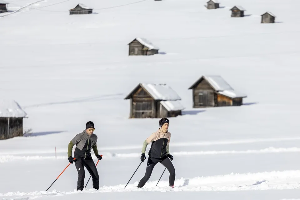 Langläufer vor schneebedeckten Hütten in Obertilliach