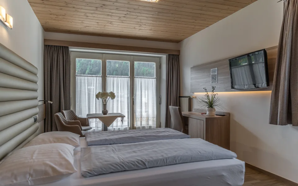 Doppelzimmer im Hotel Bergland mit Holzmöbeln und Sitzplatz am Fenster